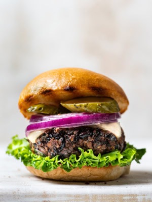 Side view of black bean burger in a bun with lettuce, pickles and sliced red onion