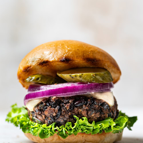 Side view of black bean burger in a bun with lettuce, pickles and sliced red onion
