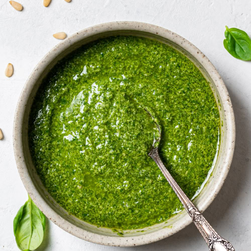 Basil Pesto in bowl with spoon and loose basil leaves around it