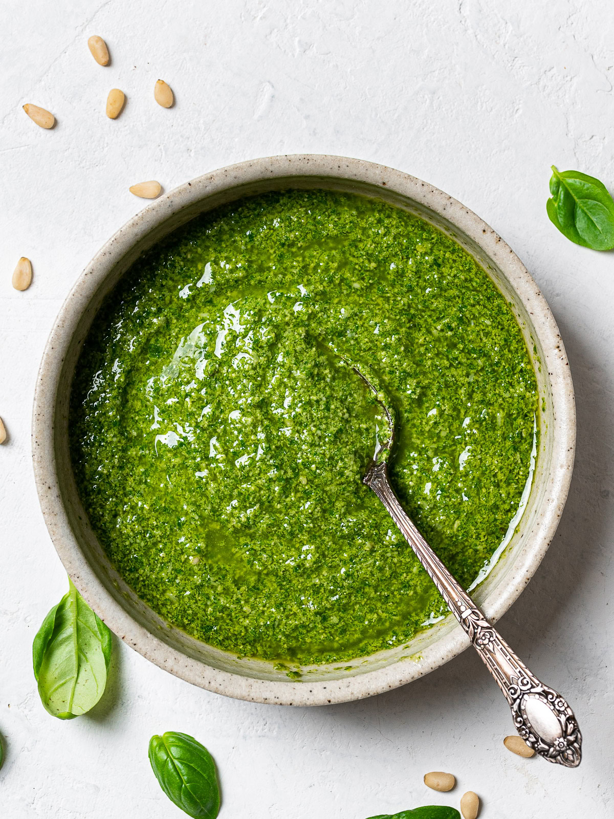 Basil Pesto in bowl with spoon and loose basil leaves around it