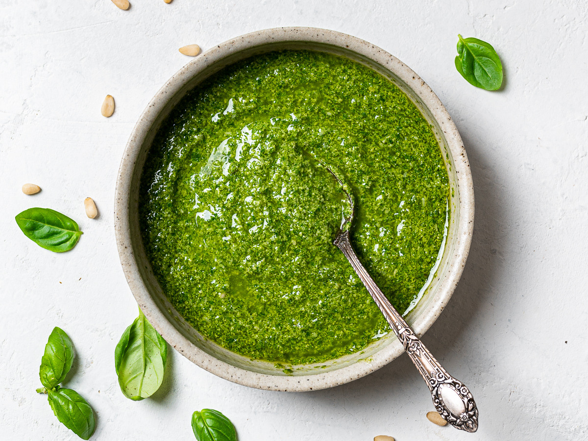 Basil Pesto in bowl with spoon and loose basil leaves around it