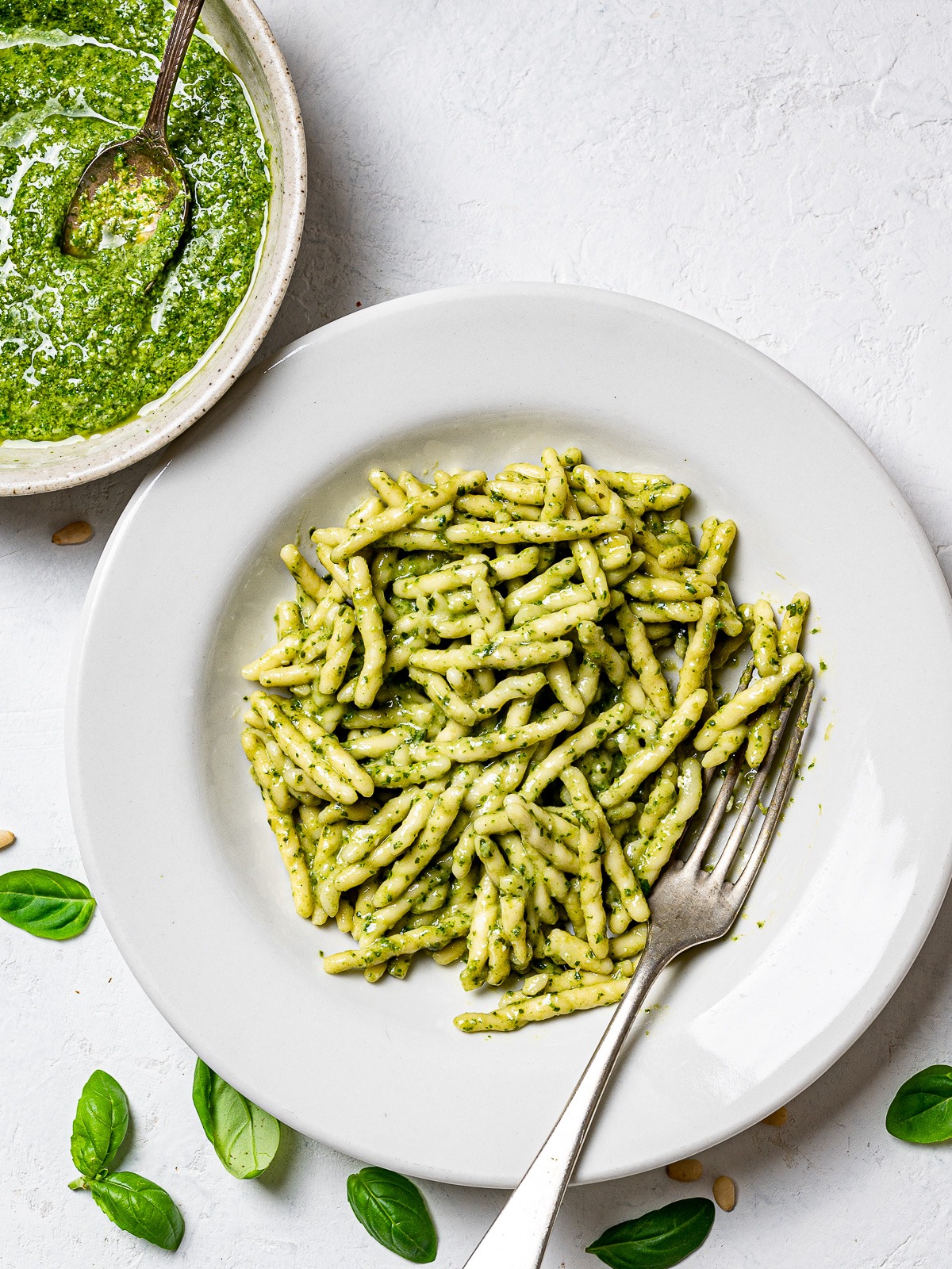 trofie pasta tossed with basil pesto in bowl and the bowl of basil pesto showing on the side