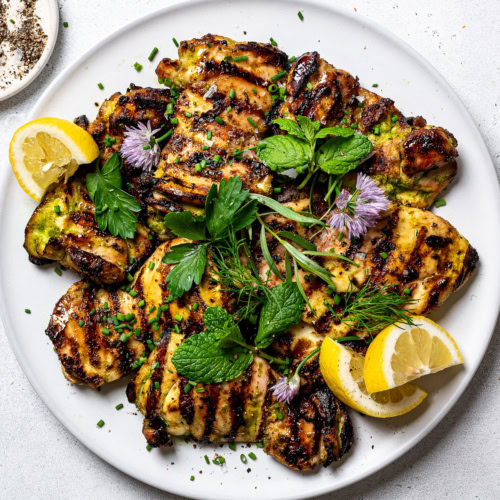 Grilled yogurt-marinated chicken on platter, garnished with hers and lemon wedges