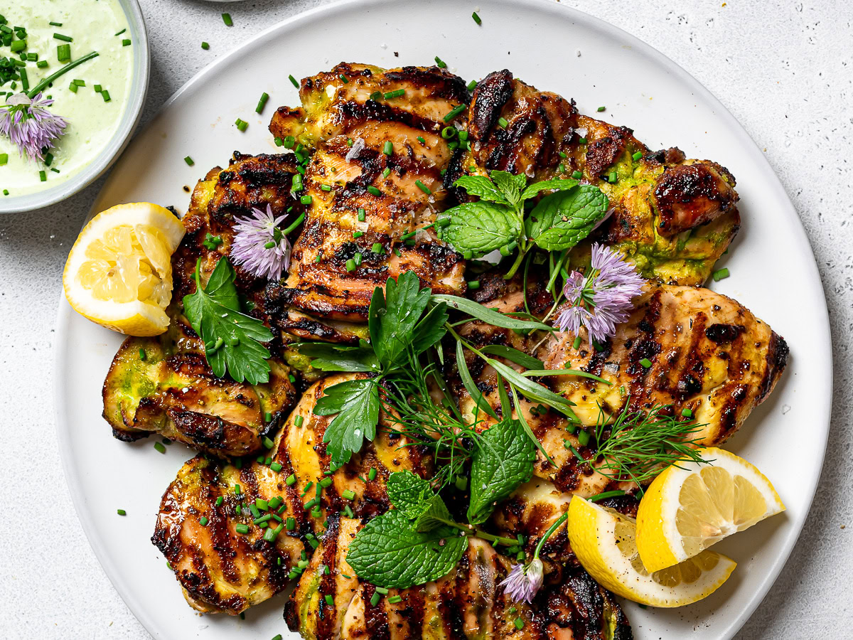 close up of Grilled yogurt-marinated chicken on platter, garnished with herbs and lemon wedges