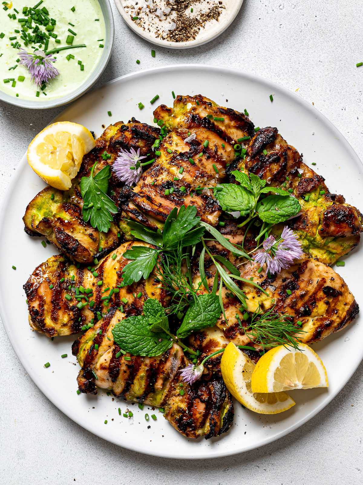 Grilled yogurt-marinated chicken on platter, garnished with herbs and lemon wedges and served with herby-yogurt sauce on the side
