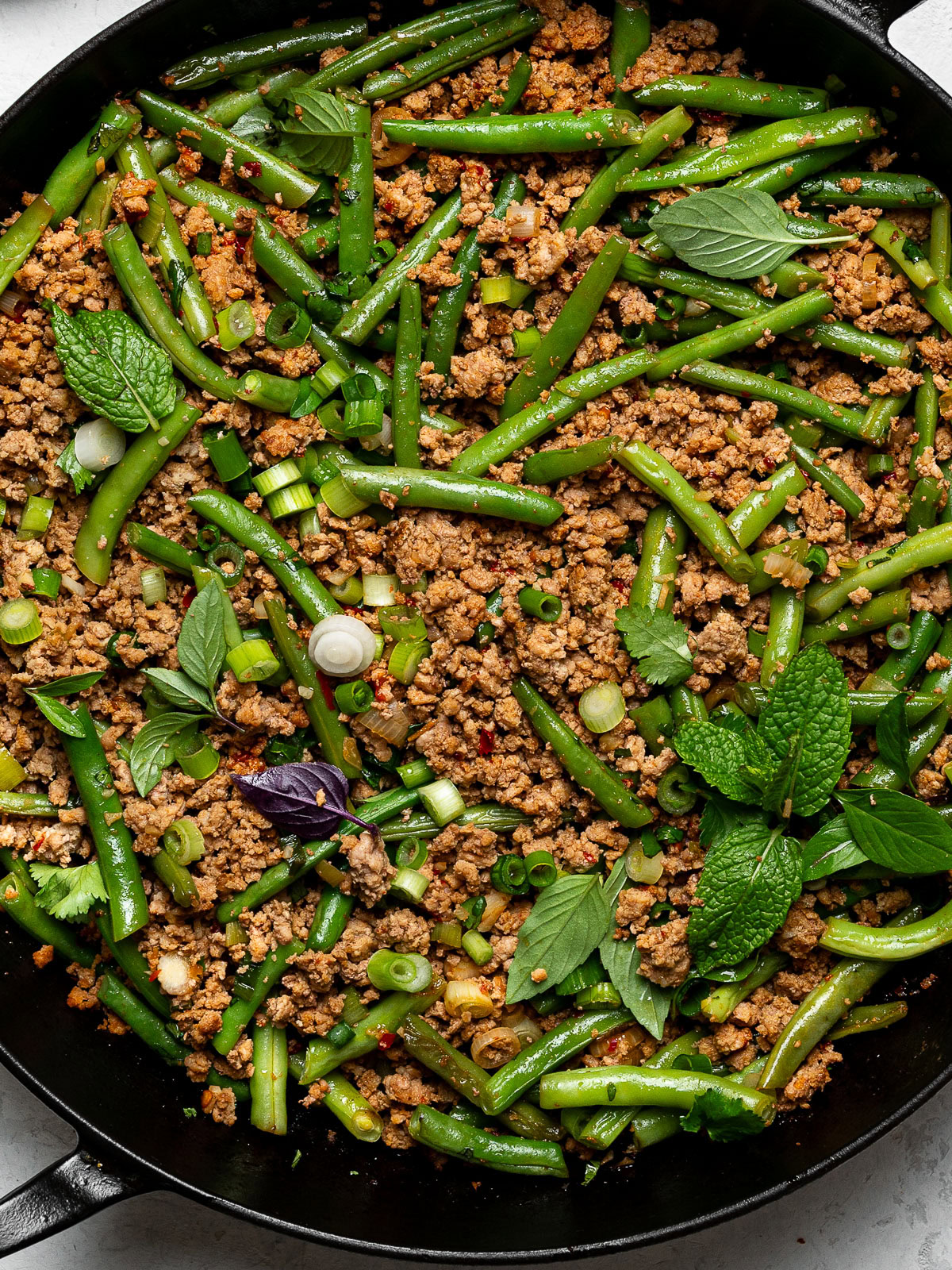 close up of turkey and green bean stir-fry in skillet garnished with herbs