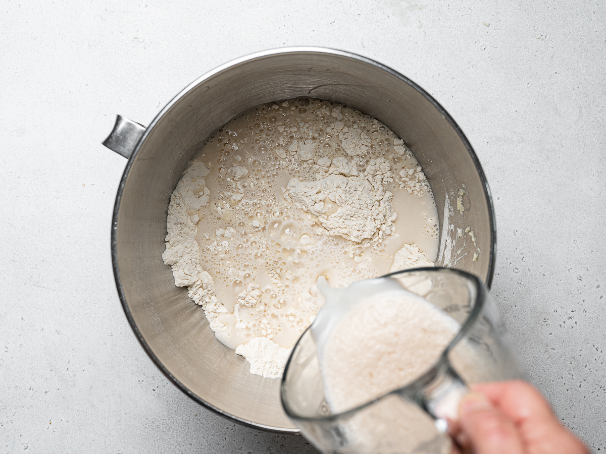 pouring yeast mixture into mixing bowl with flour
