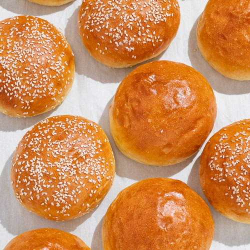 top view of many baked Light brioche buns in a row -some with sesame seeds and some without