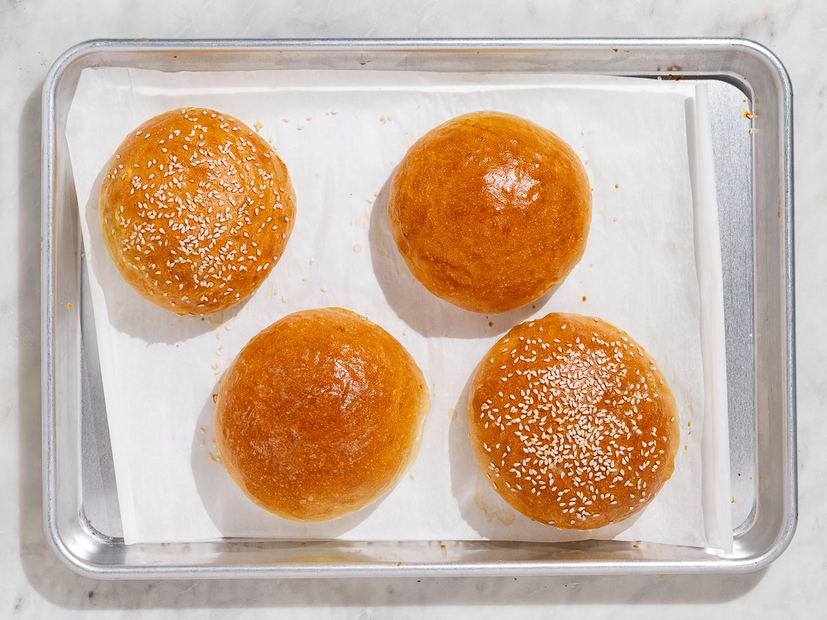 four baked hamburger buns on baking sheet