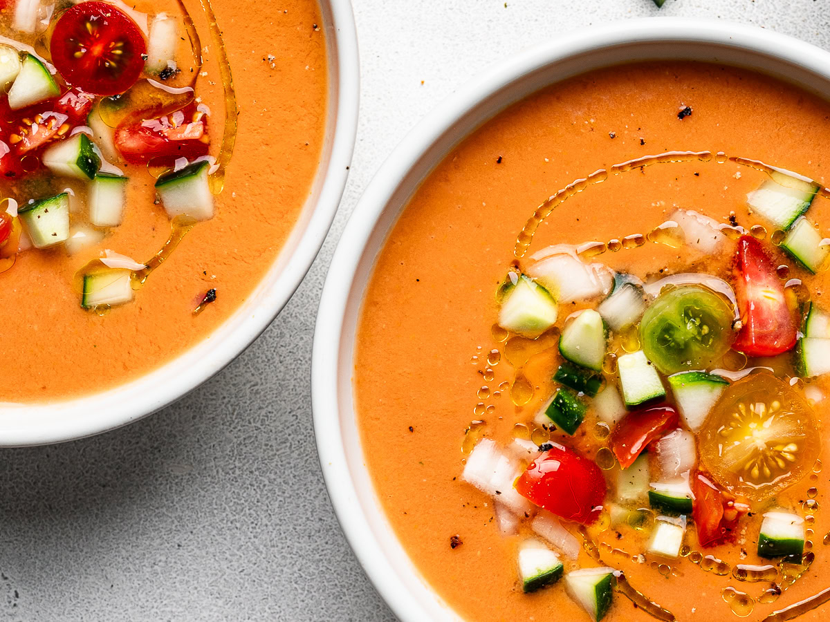 close up of Gazpacho served in two white soup in bowls topped with garnishes