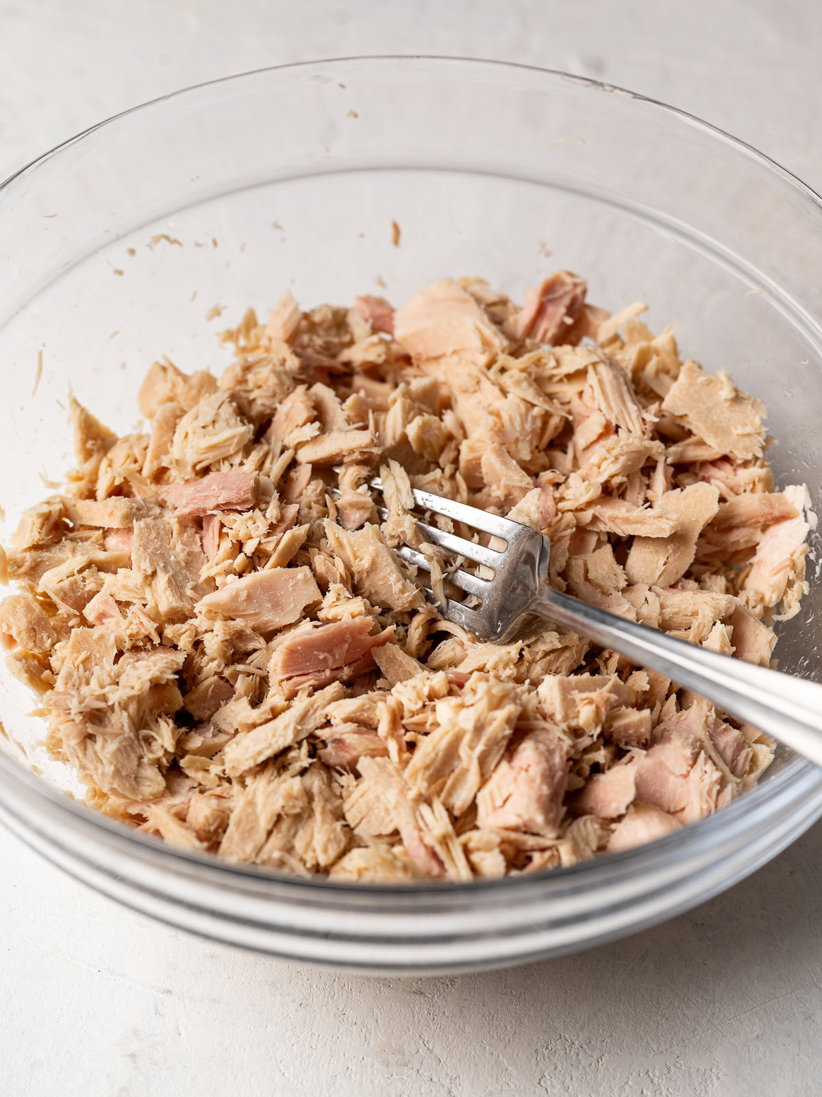 flaking the tuna in a bowl with a fork 