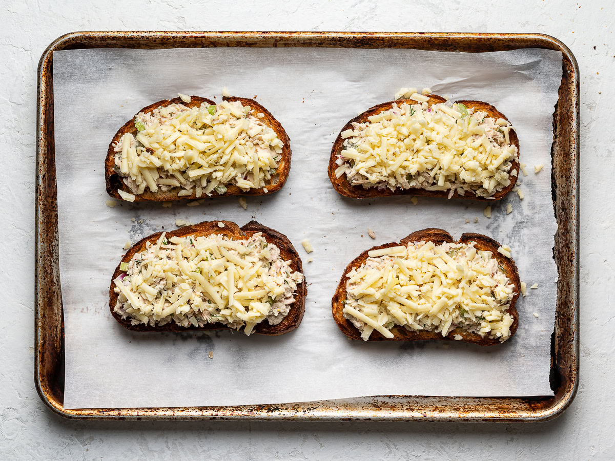 4 toasts on baking sheet topped with tuna salad and grated cheese