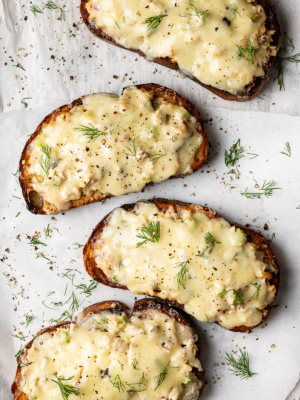 4 open-faced tuna melt toasts with melted cheese on baking sheet garnished with dill and black pepper