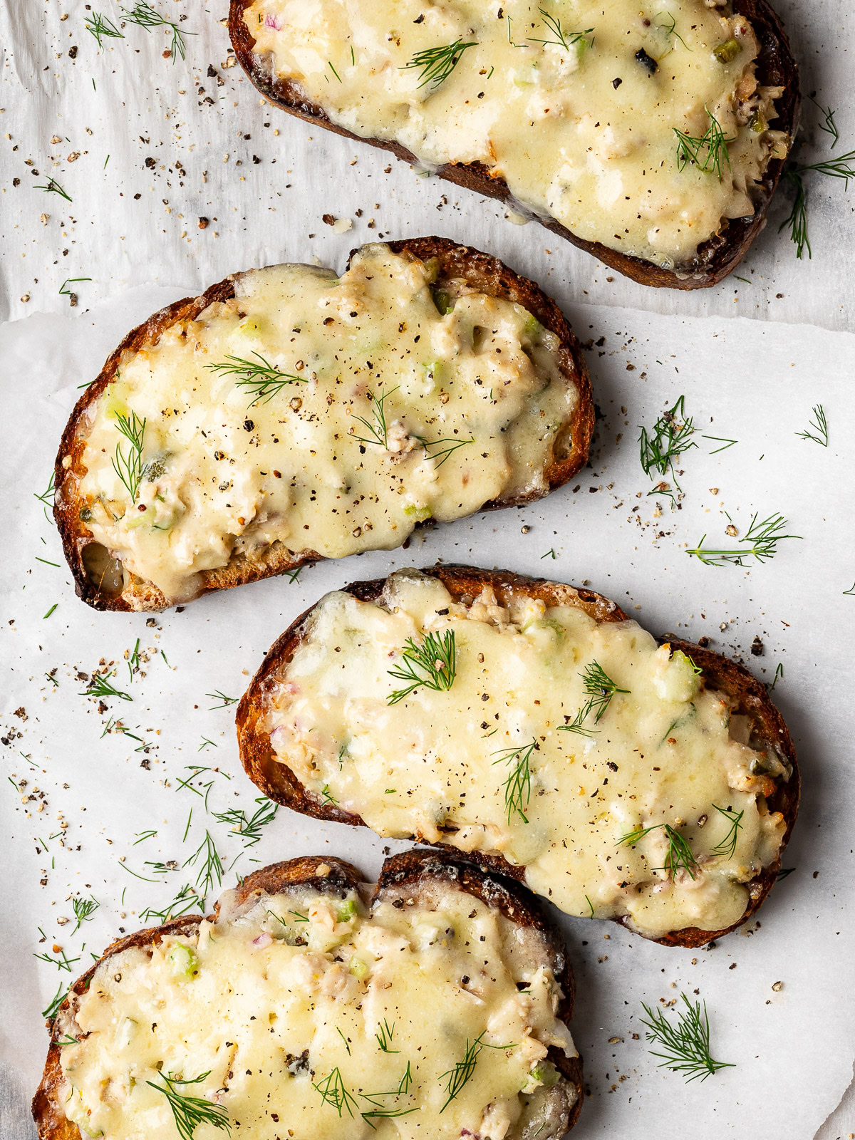 4 open-faced tuna melt toasts with melted cheese on baking sheet garnished with dill and black pepper