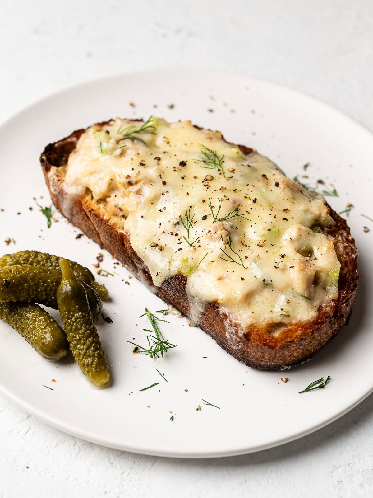 One tuna melt served on a plate with gherkins on the side