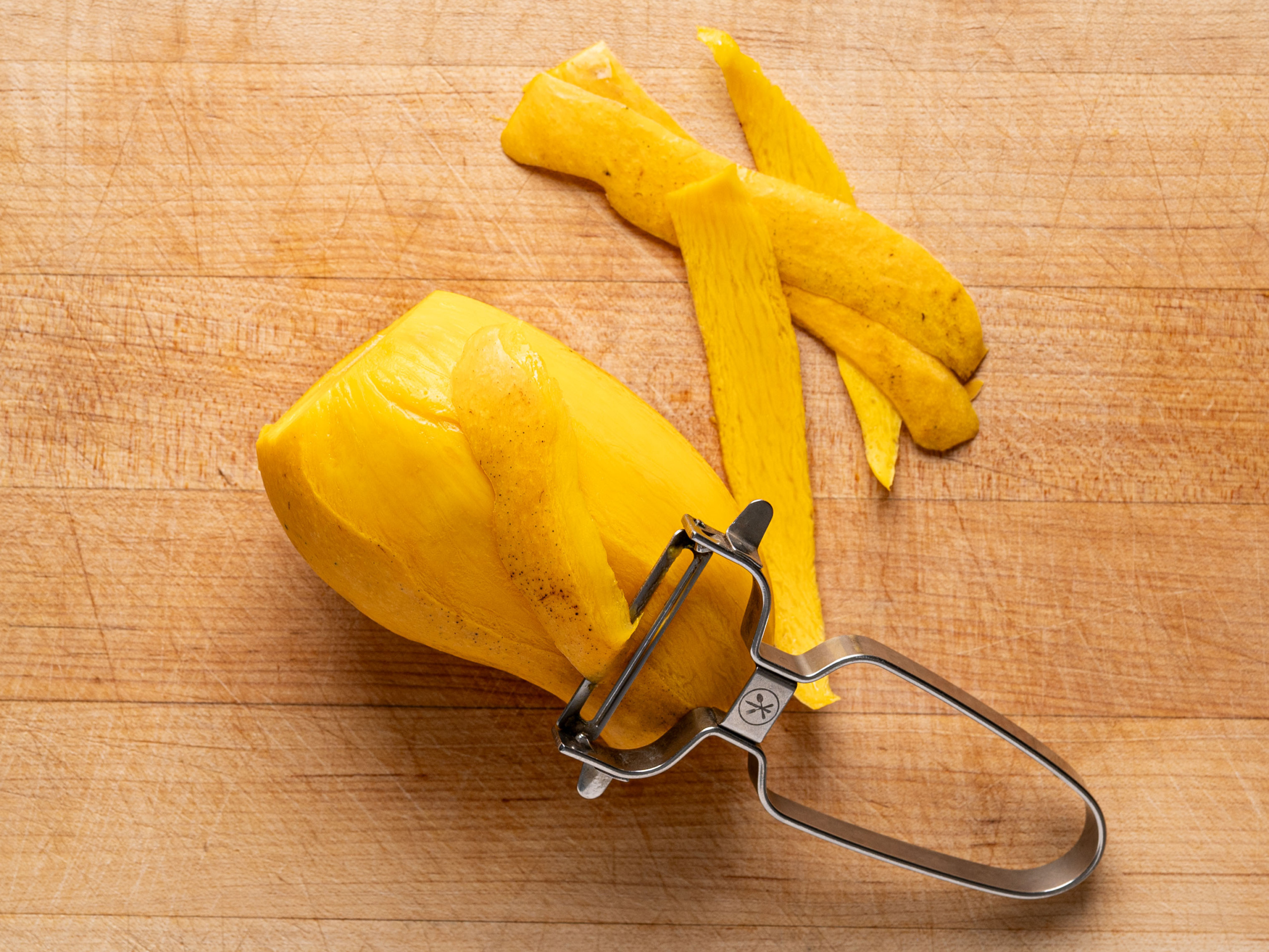 peeling a mango with vegetable peeler on cutting board