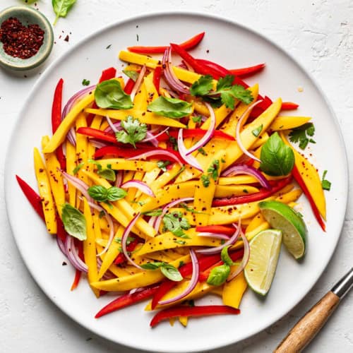 Mango salad served on white platter with small bowl of Aleppo pepper on the side