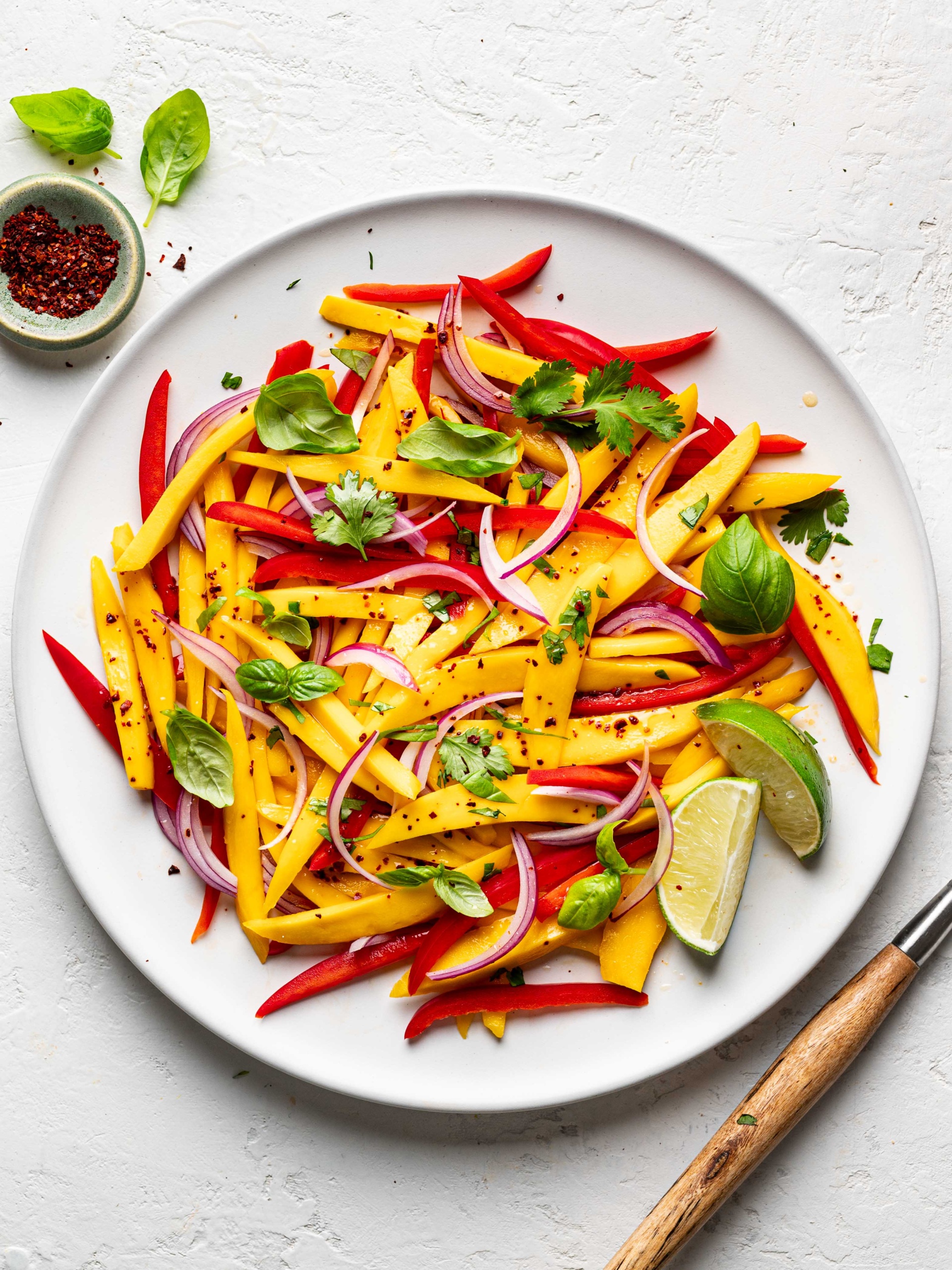 Mango salad served on white platter with small bowl of Aleppo pepper on the side