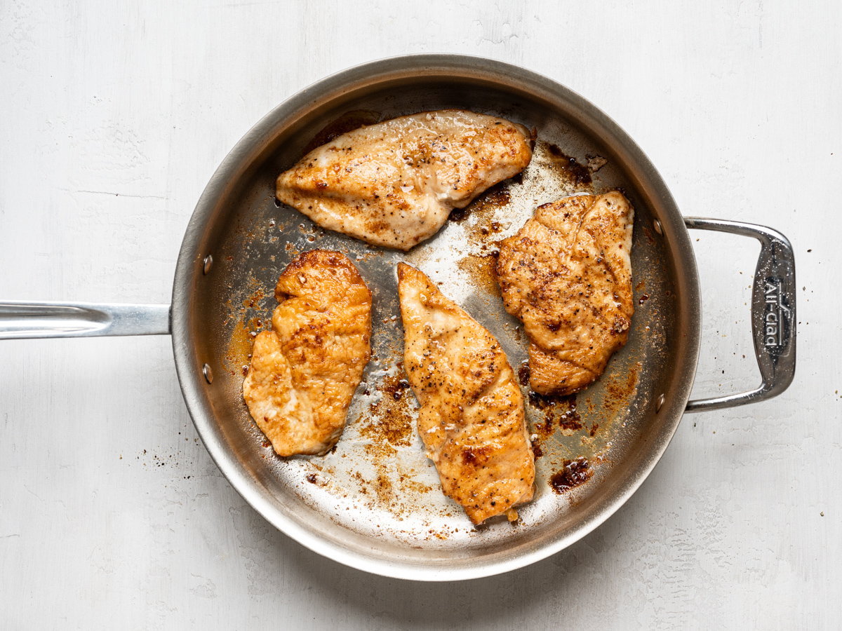browning 4 chicken pieces in a stainless steel skillet