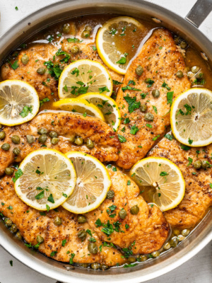 close-up of finished chicken piccata dish in skillet, garnished with lemon slices and chopped parsley