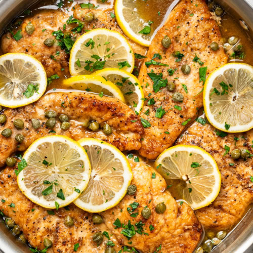close-up of finished chicken piccata dish in skillet, garnished with lemon slices and chopped parsley