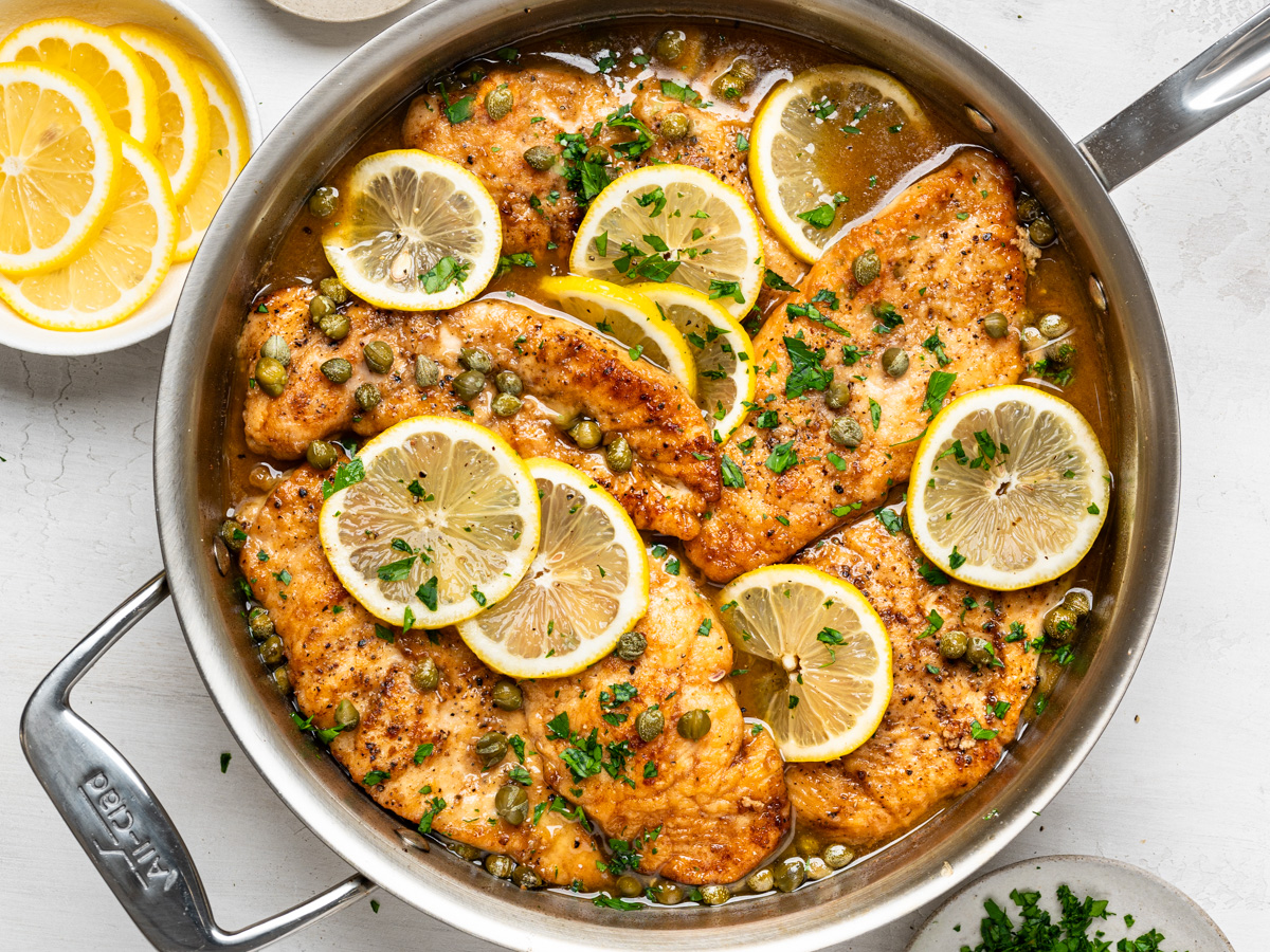 finished chicken piccata dish in skillet, shown with garnish bowls on the side
