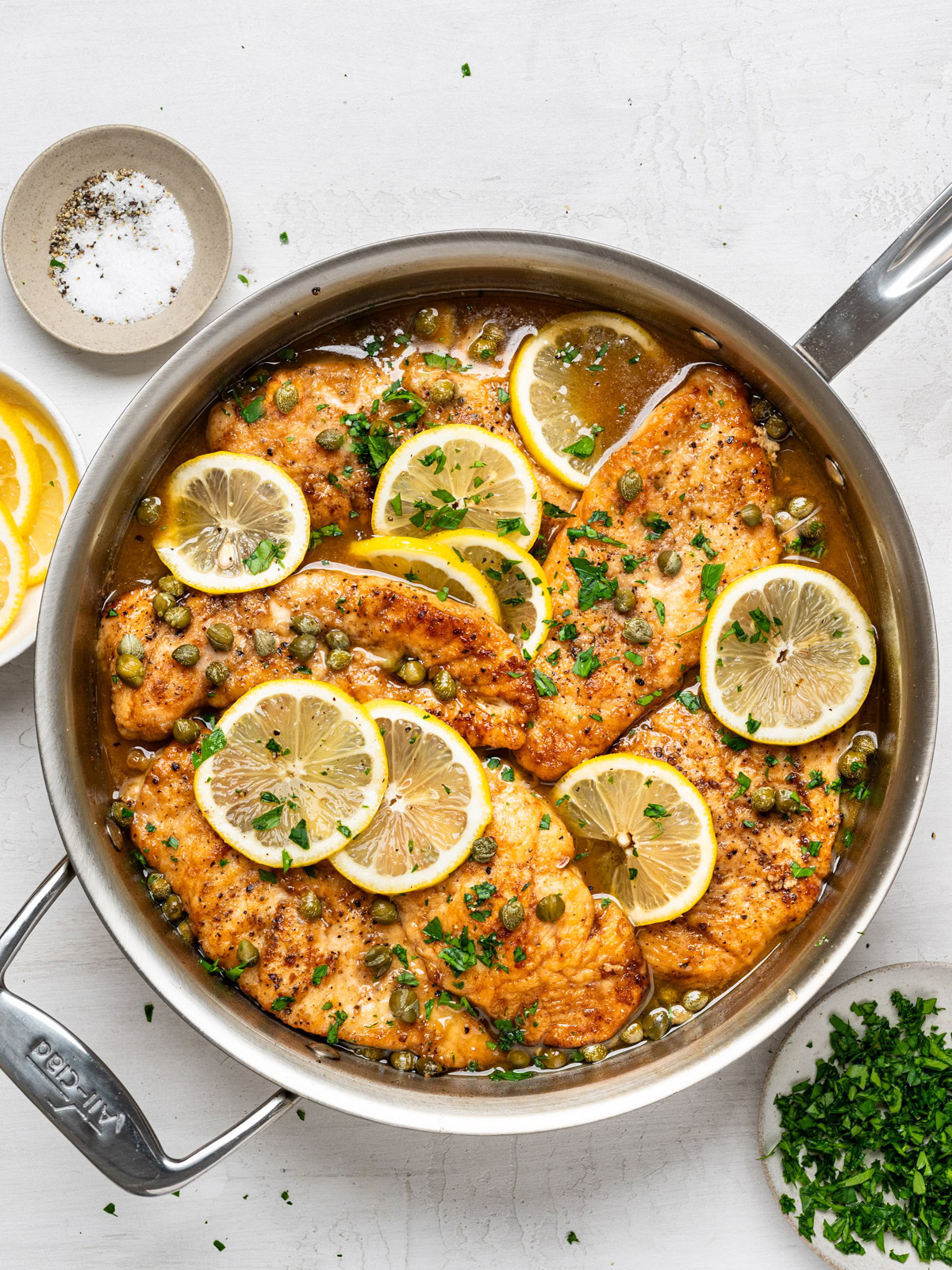 finished chicken piccata dish in skillet, shown with garnish bowls on the side