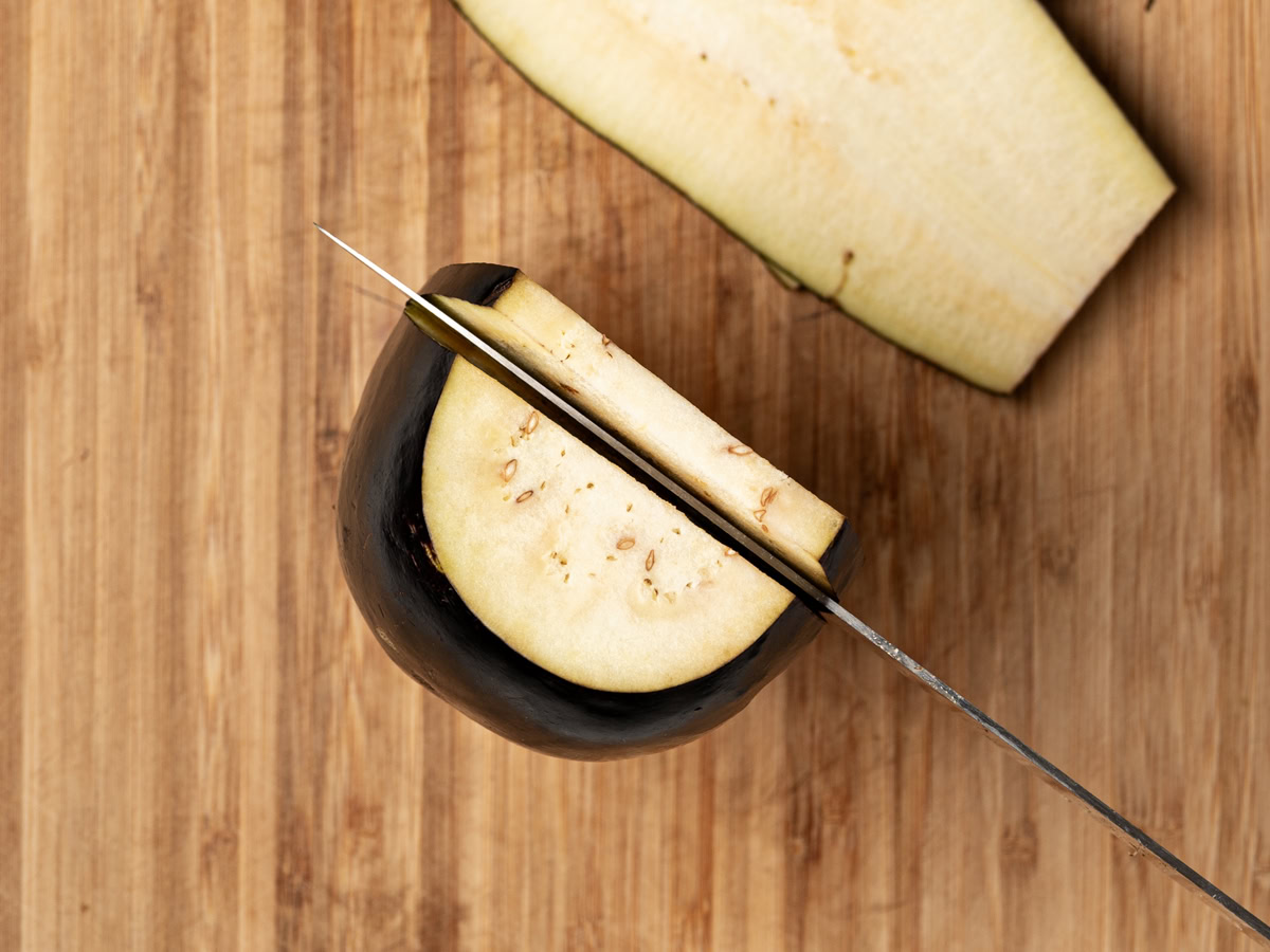 top-view of a knife slicing an  eggplant into 1/4-inch slices