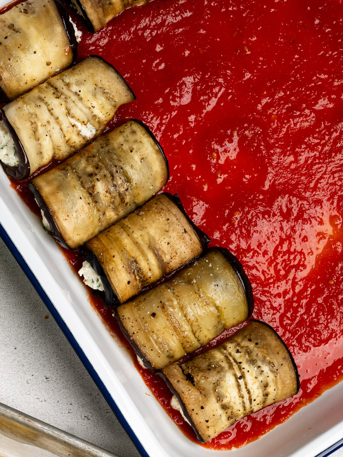 a few rolled eggplant bundles in casserole dish with tomato sauce