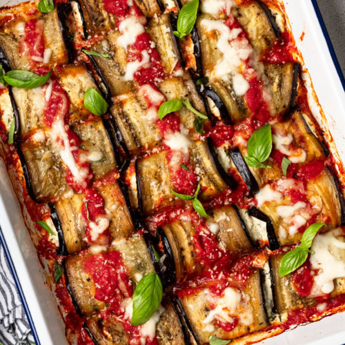 A casserole of baked eggplant rollatini garnished with fresh basil leaves