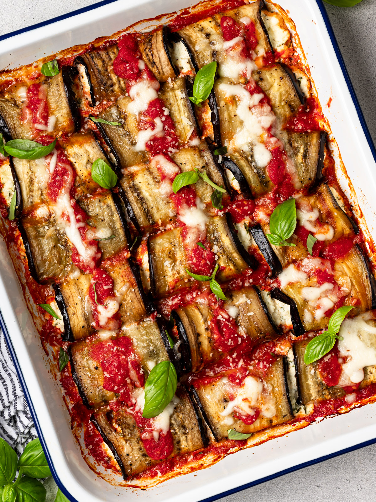 A casserole of baked eggplant rollatini garnished with fresh basil leaves