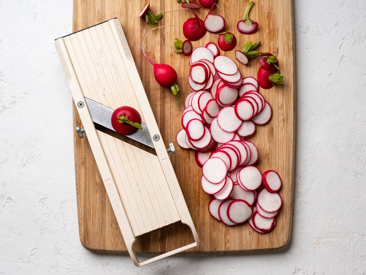 slicing radishes with mandoline on cutting board