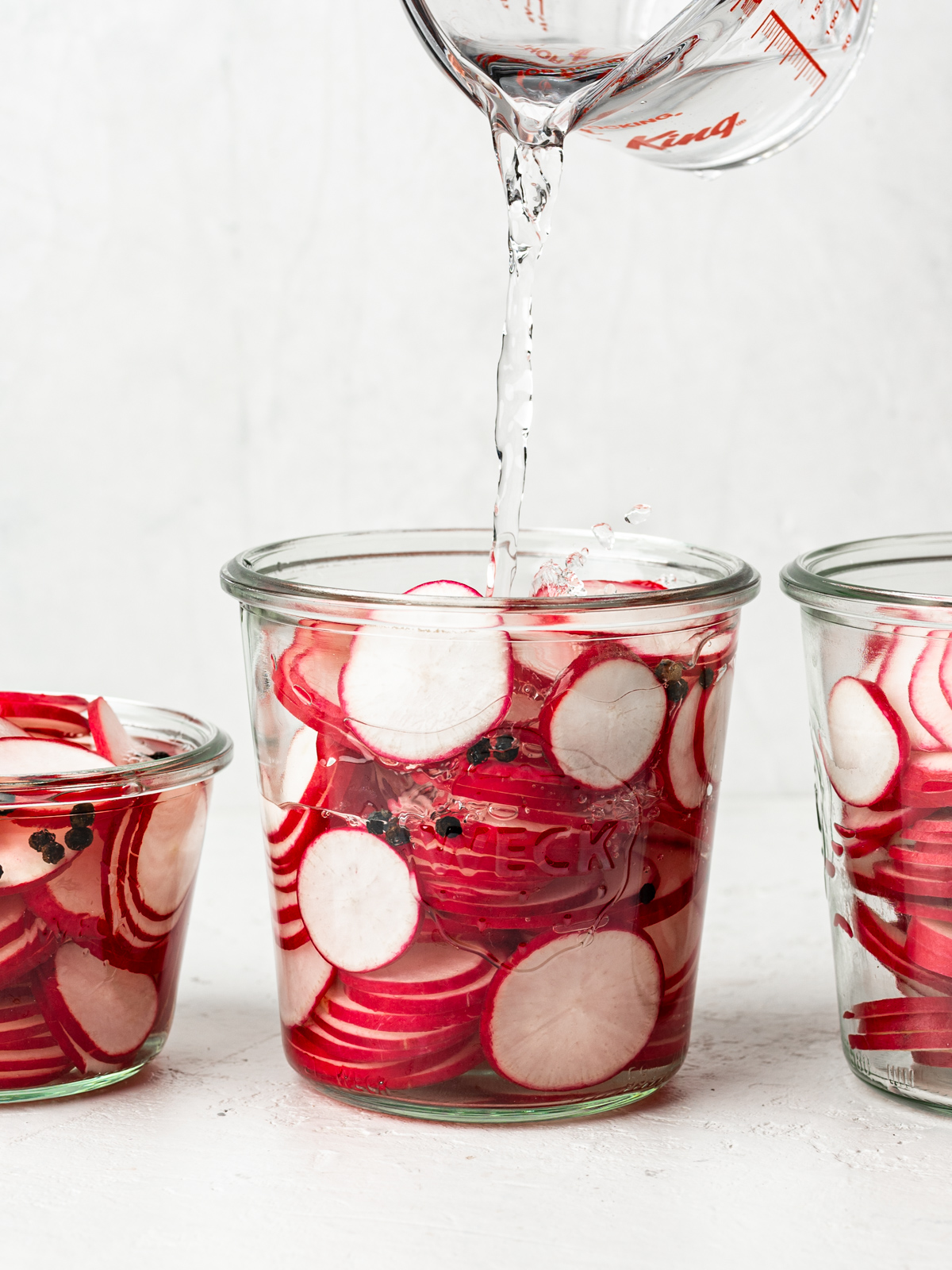 pouring pickling liquid into jars with sliced radishes