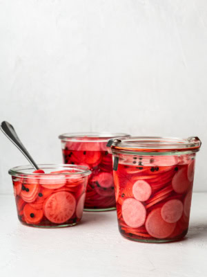 vertical image of 3 jars filled with pickled radishes