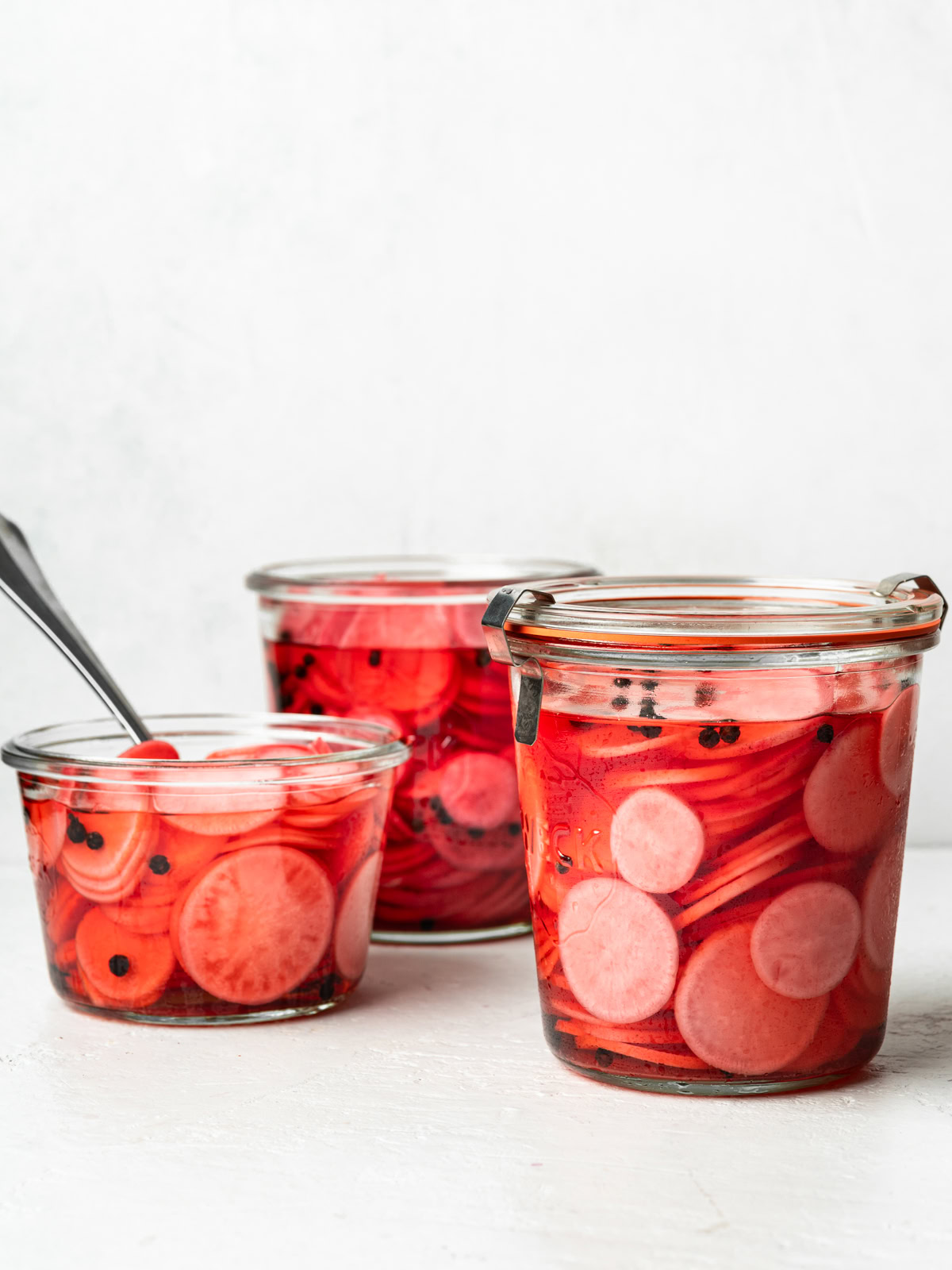 vertical image of 3 jars filled with pickled radishes