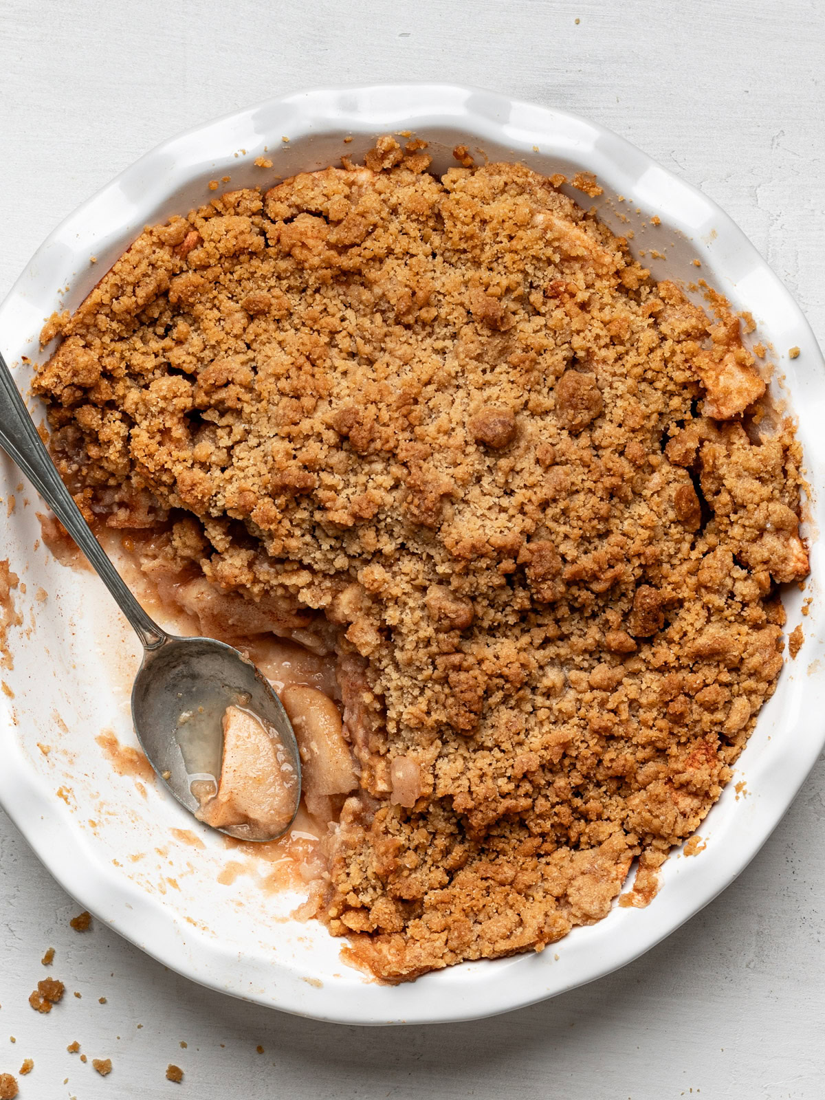 top view of apple crisp without oats in pie dish with spoon and a piece missing