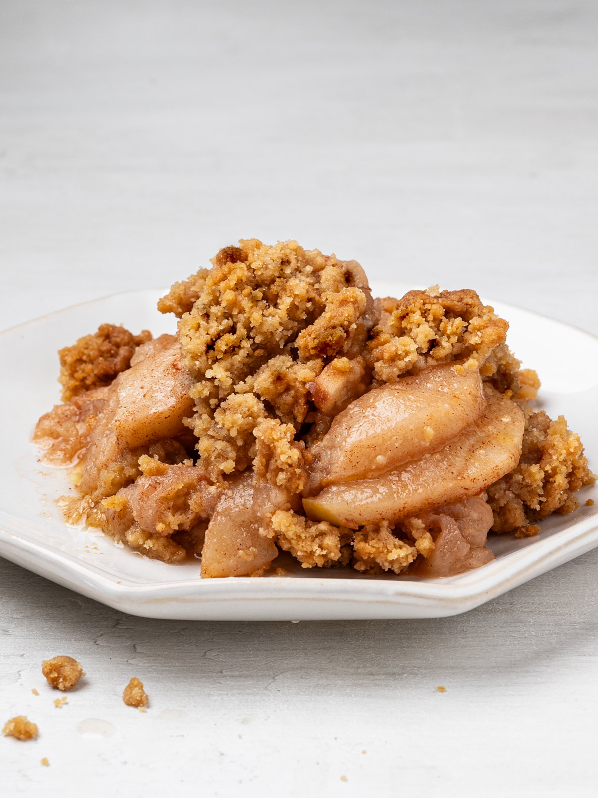 A side view of a serving of apple crisp without oats on a white plate