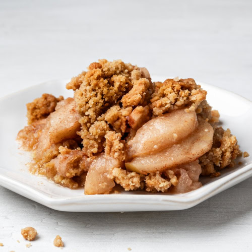 A side view of a serving of apple crisp without oats on a white plate