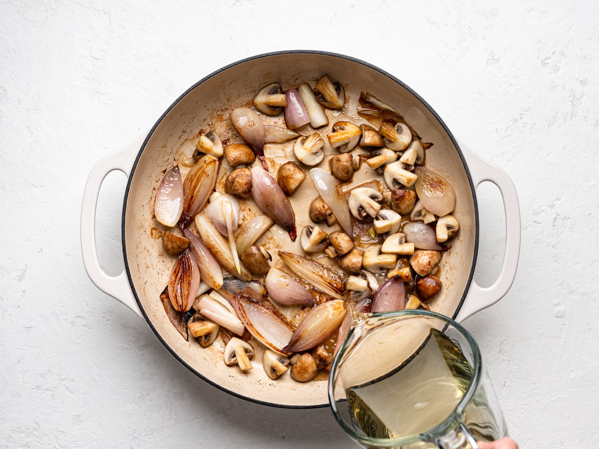 pouring in wine from a measuring cup into skillet with shallot-mushroom mixture