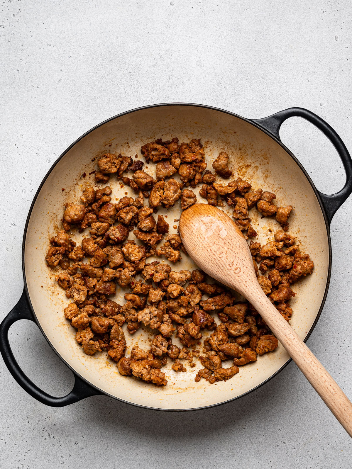 sautéed pieces of sausage in skillet with wooden spoon