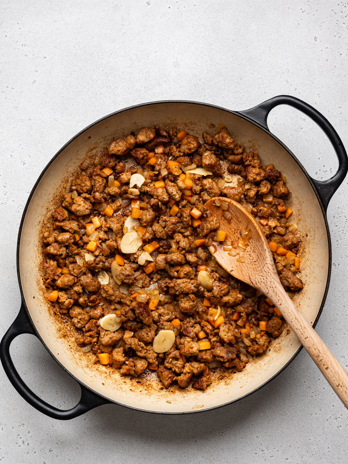 sautéed pieces of sausage with carrots, onion and garlic in skillet with wooden spoon