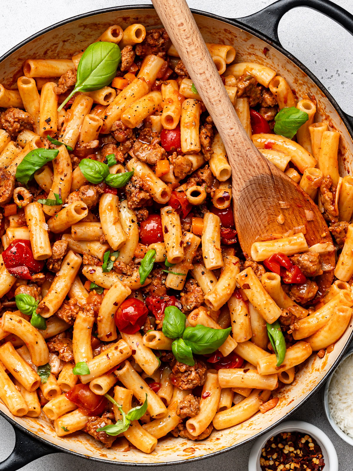 Spicy Italian sausage pasta dish combined in skillet and garnished with fresh basil