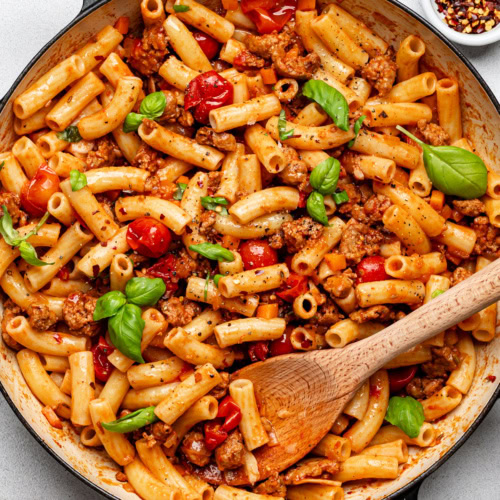 Spicy Italian sausage pasta dish combined in skillet and garnished with fresh basil