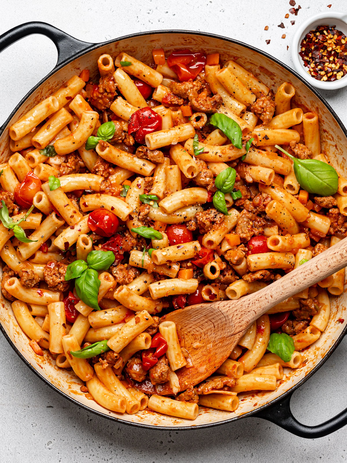 Spicy Italian sausage pasta dish combined in skillet and garnished with fresh basil 