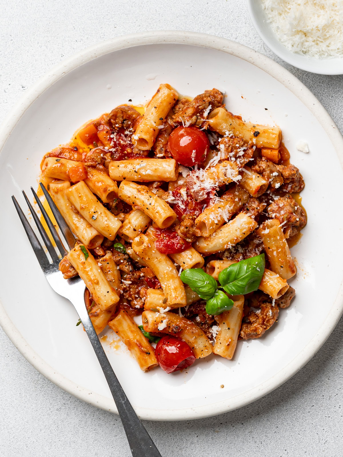 Spicy Italian Sausage pasta served on a white plate with a bowl of parmesan cheese on the side. 