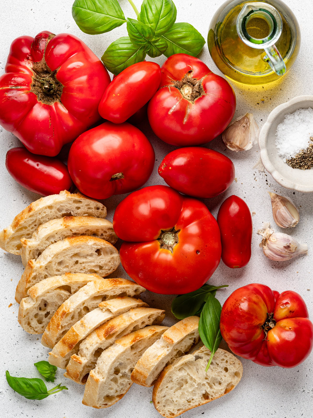 fresh tomatoes, bread slices and other ingredients laid out on a light-coloured board