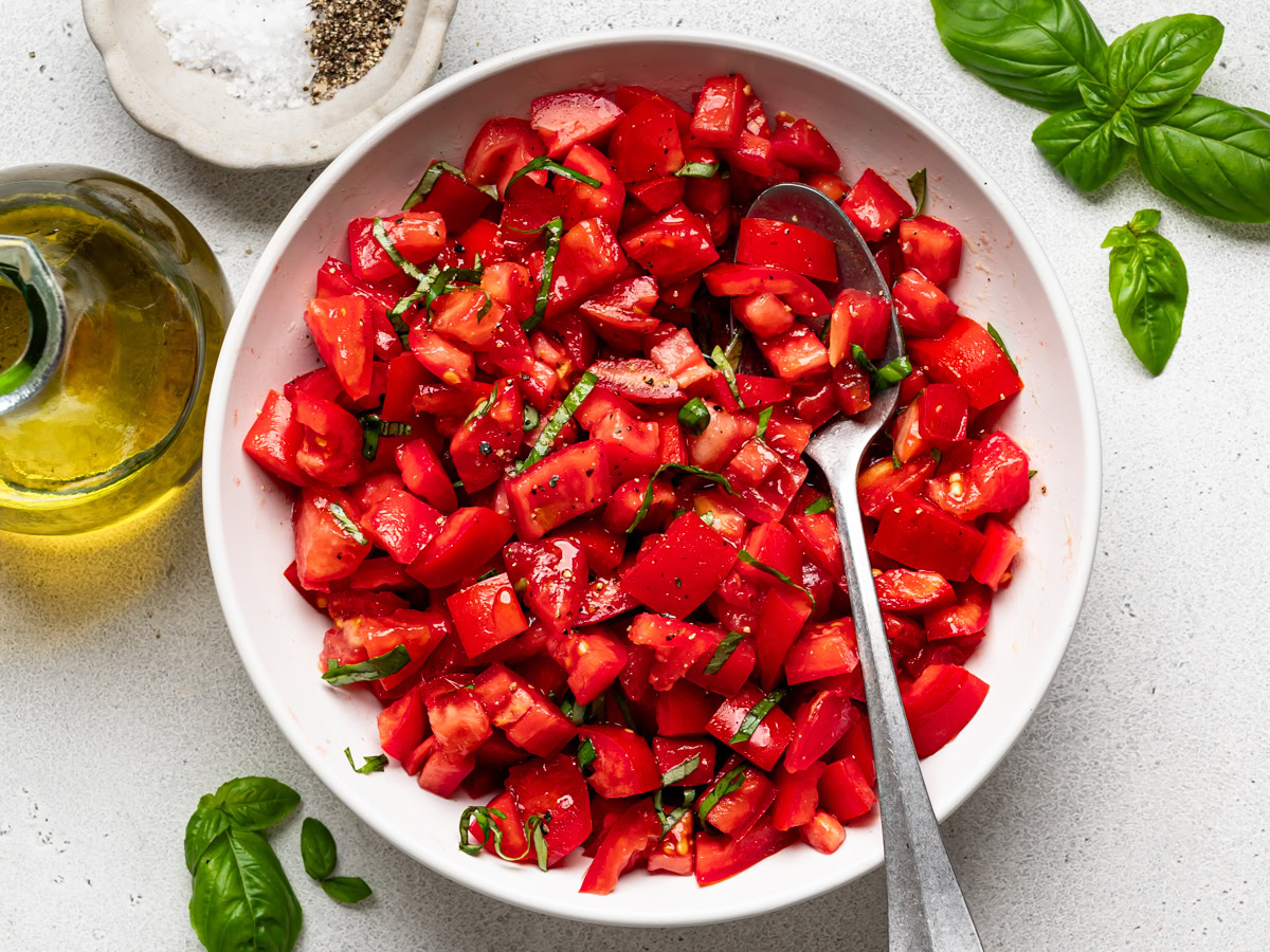 tomato mixture in a white bowl with olive oil, salt and pepper bowl on the side