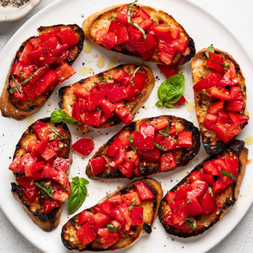 prepared bruschetta al pomodoro served on a white platter with a small bowl of salt and pepper on the side