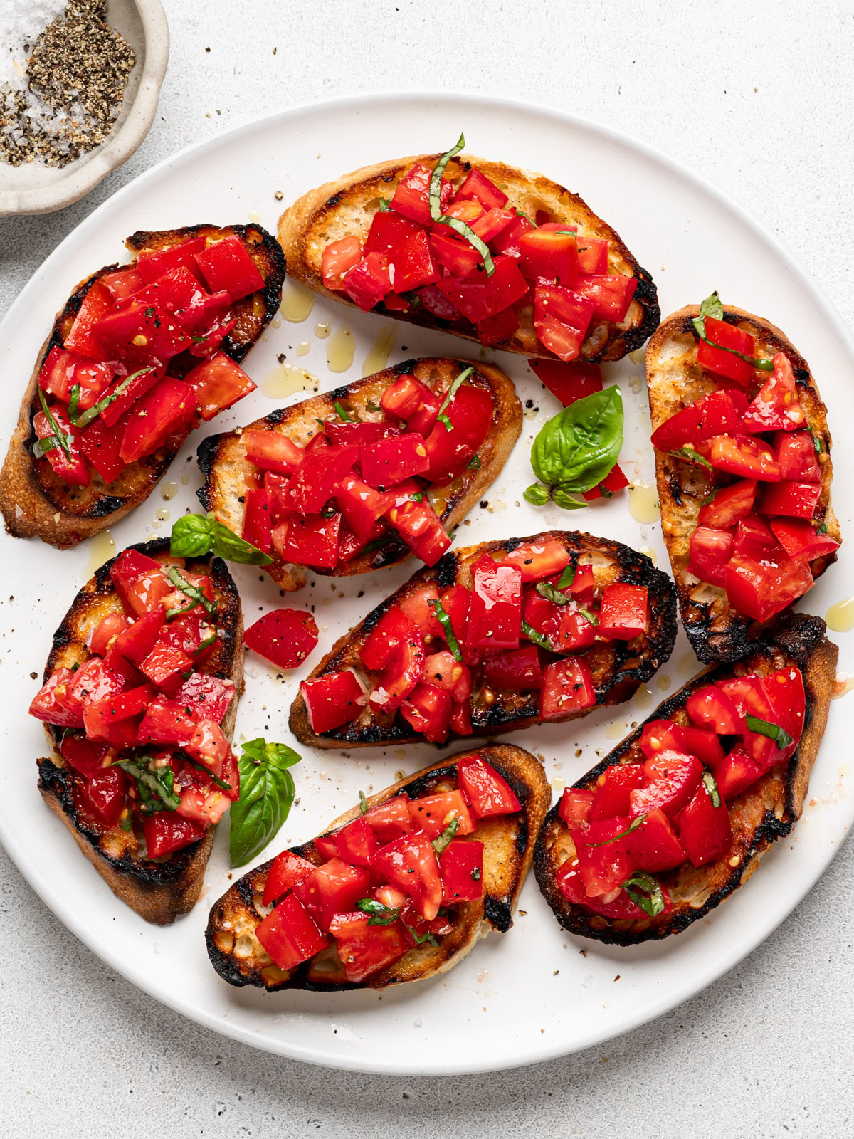 prepared bruschetta al pomodoro served on a white platter with a small bowl of salt and pepper on the side