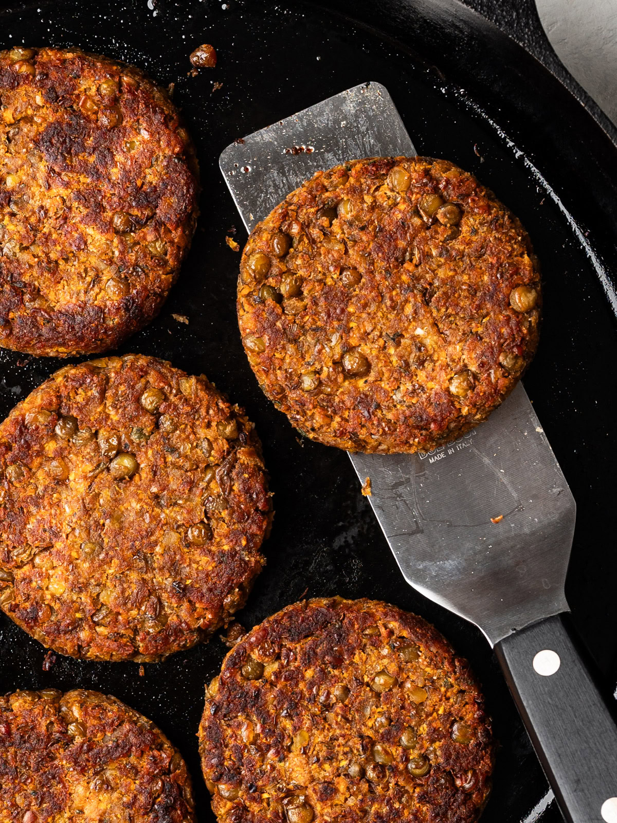 close-up of a spatula holding a patty in skillet